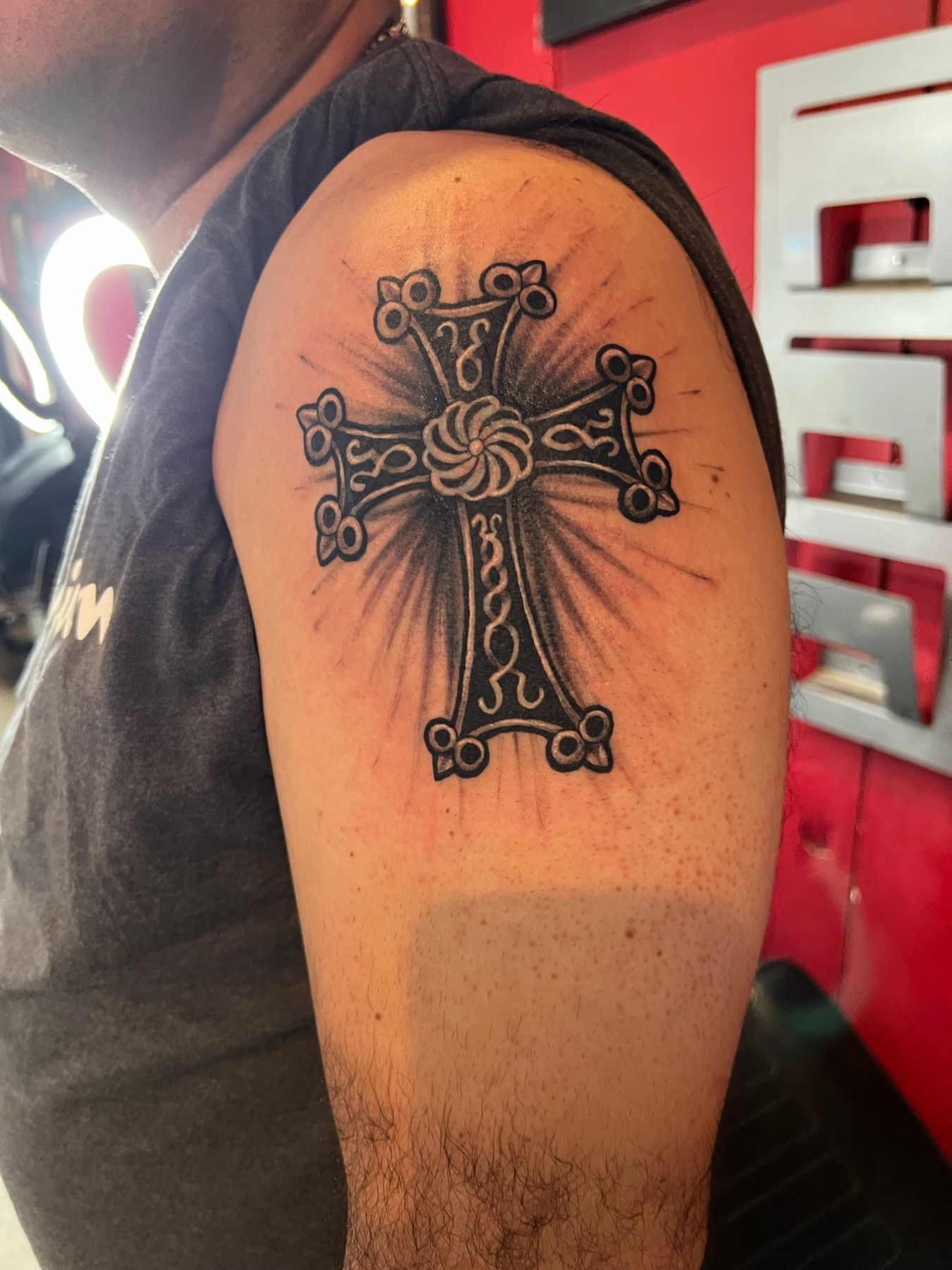 Finished ornate black and grey cross cover-up with radiating rays on the upper arm, by American Ink in Sherman Oaks.