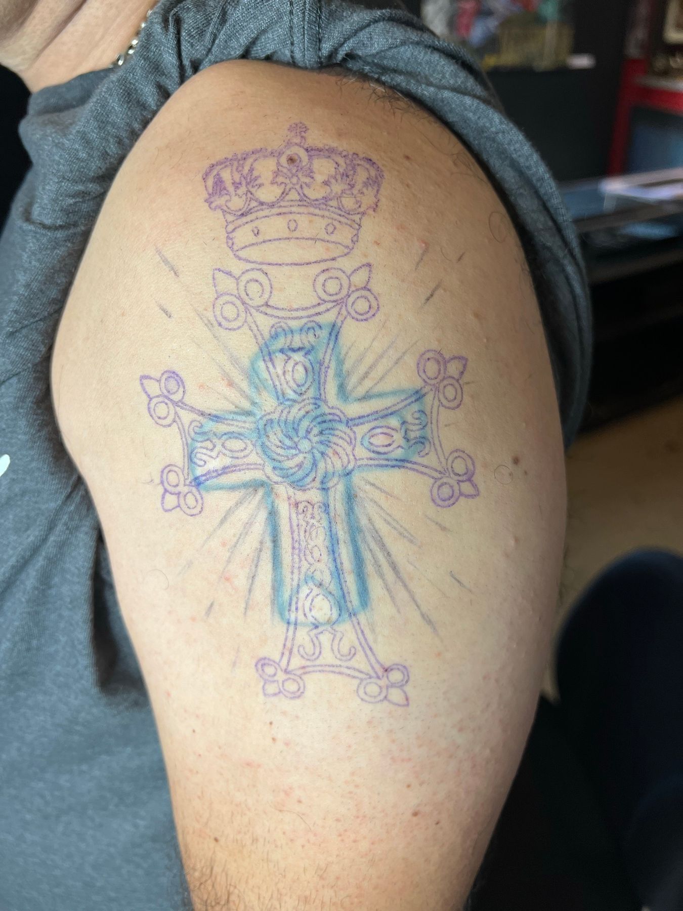 Old faded blue cross tattoo with a new ornate cross and crown design stenciled over it for a cover-up at American Ink in Sherman Oaks.