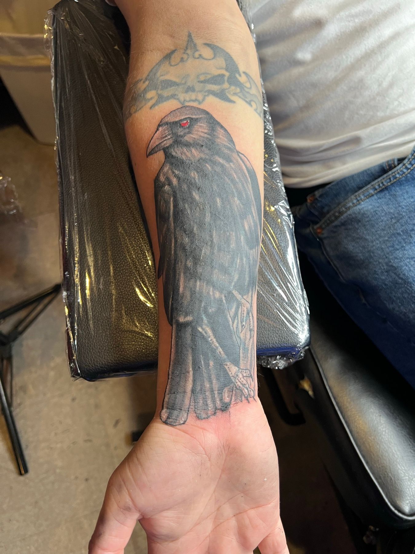 Finished black and grey raven cover-up tattoo concealing the old name on the forearm, by American Ink in Sherman Oaks.