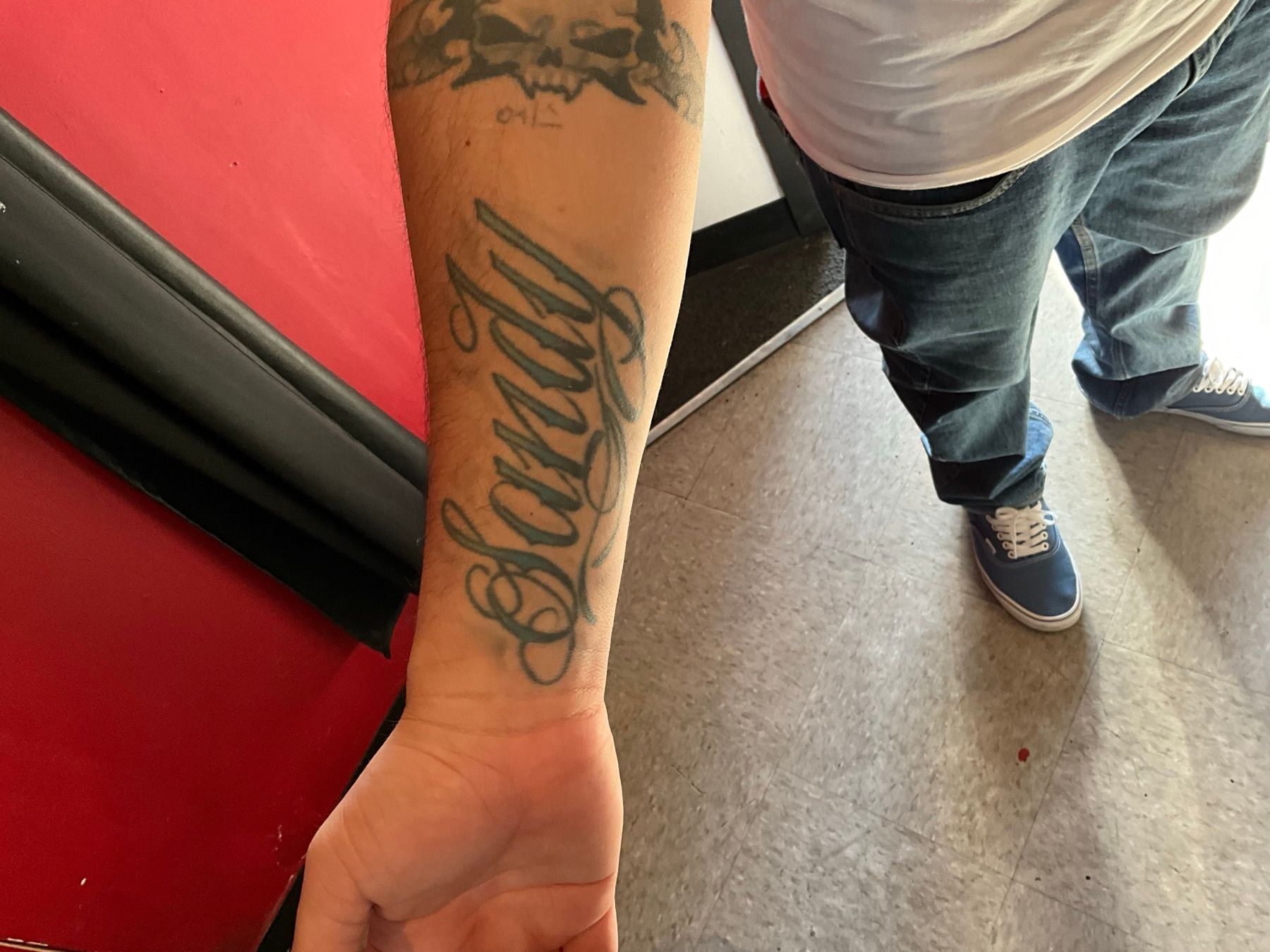 Old green script name tattoo on the forearm before its cover-up at American Ink in Sherman Oaks.