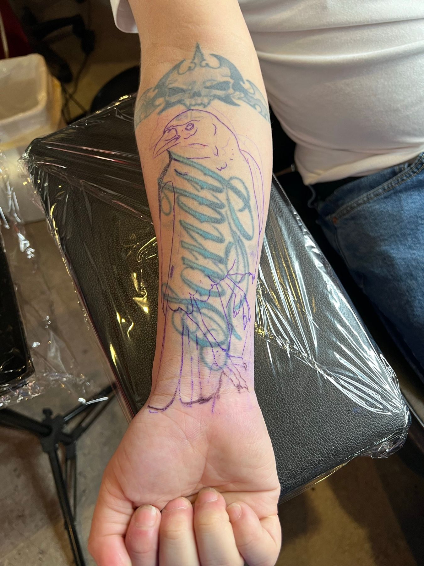 Purple crow stencil drawn over the old forearm name tattoo to plan the cover-up at American Ink in Sherman Oaks.