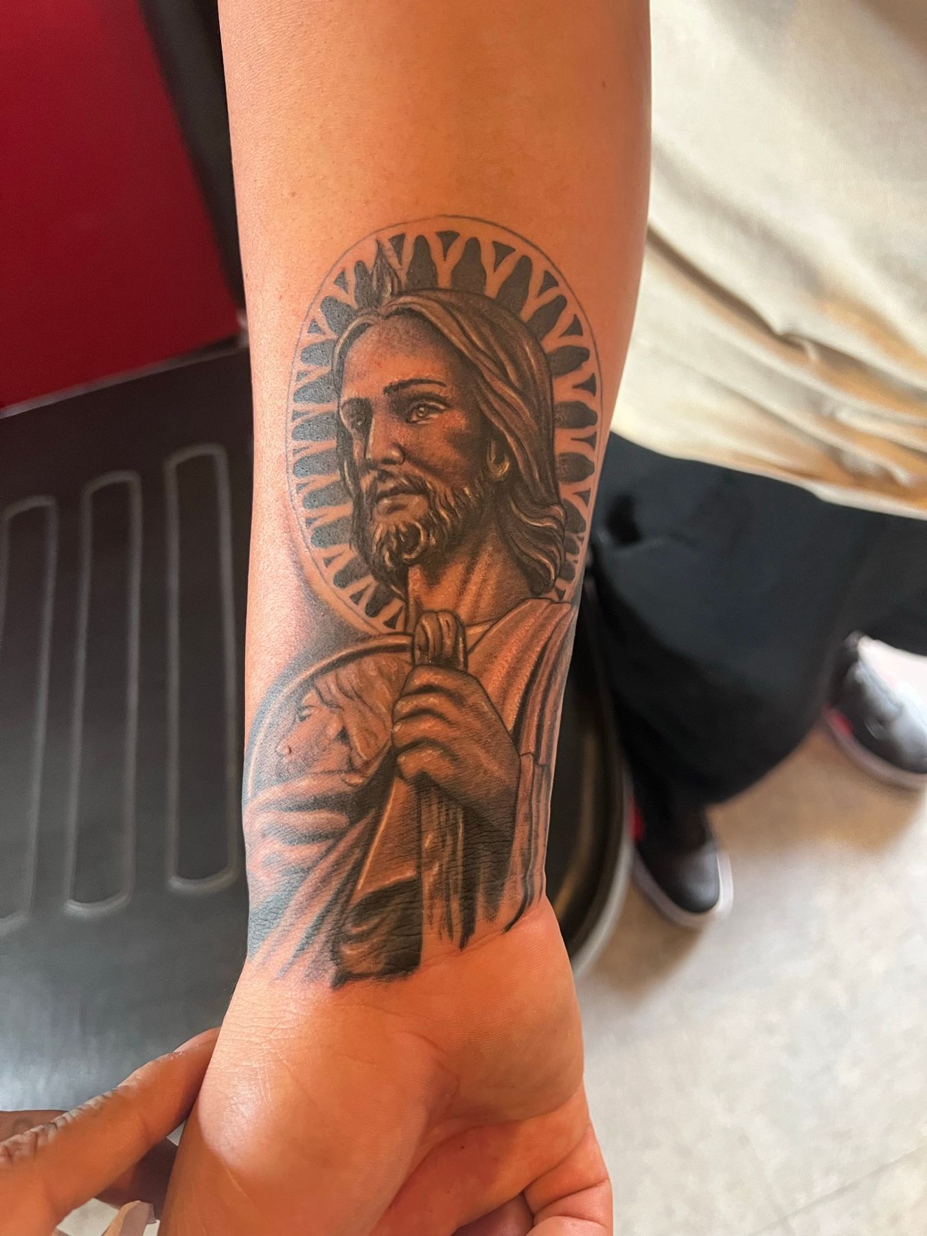 Close-up of the reworked black and grey saint portrait with a radiant halo on the forearm, at American Ink in Sherman Oaks.