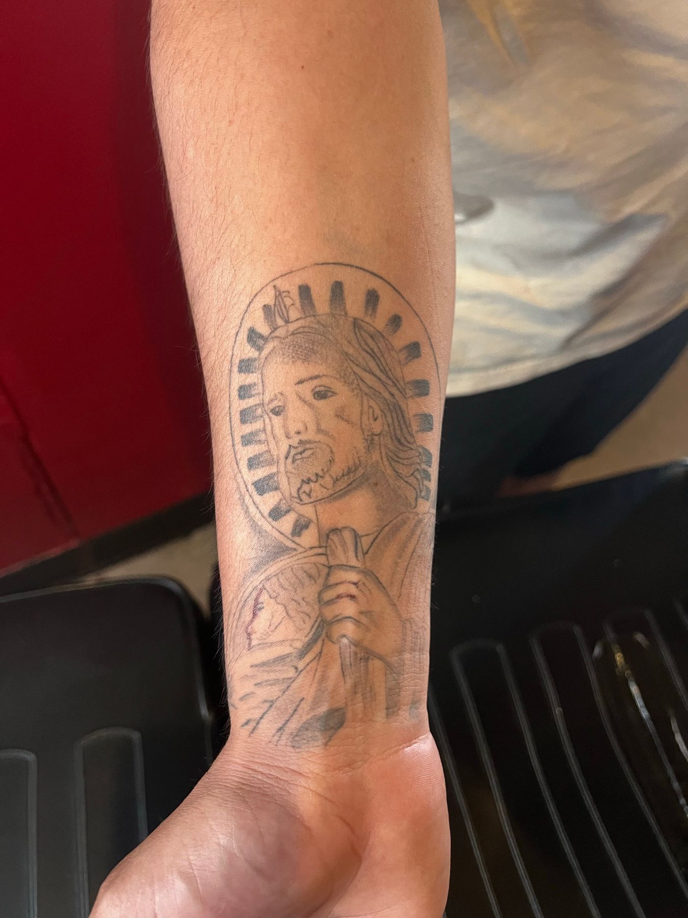 Faded black and grey religious portrait tattoo on the forearm before being reworked at American Ink in Sherman Oaks.