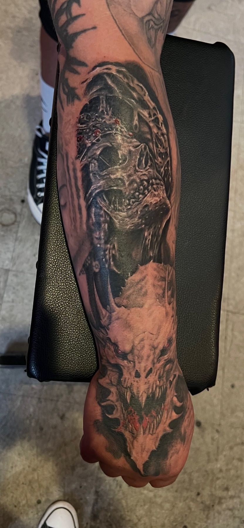 Black and grey realism tattoo of a horned demon skull with red eyes running down a forearm to the hand, by American Ink in Sherman Oaks.