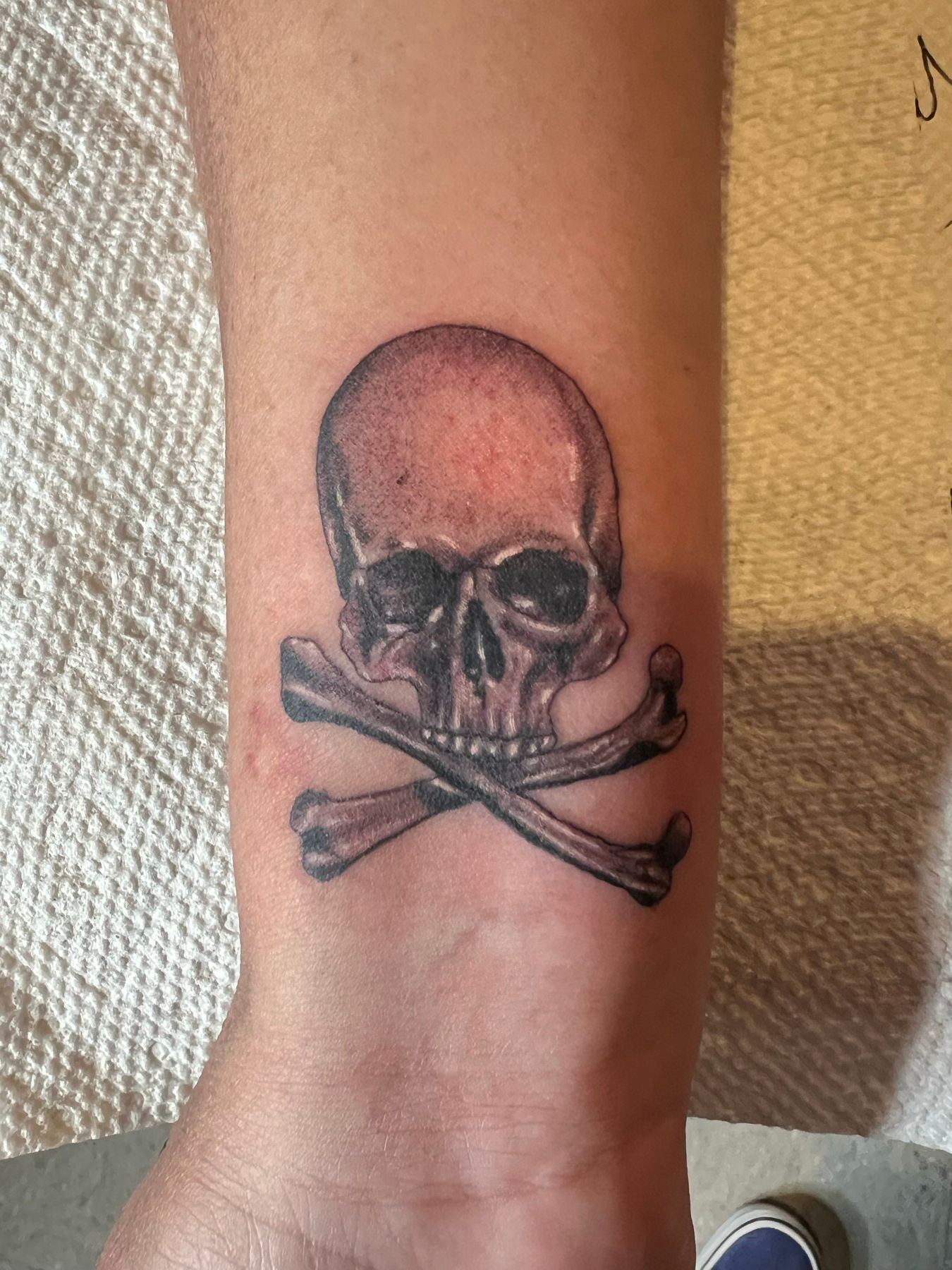 Black and grey realism tattoo of a skull and crossbones on a forearm near the wrist, by American Ink in Sherman Oaks.