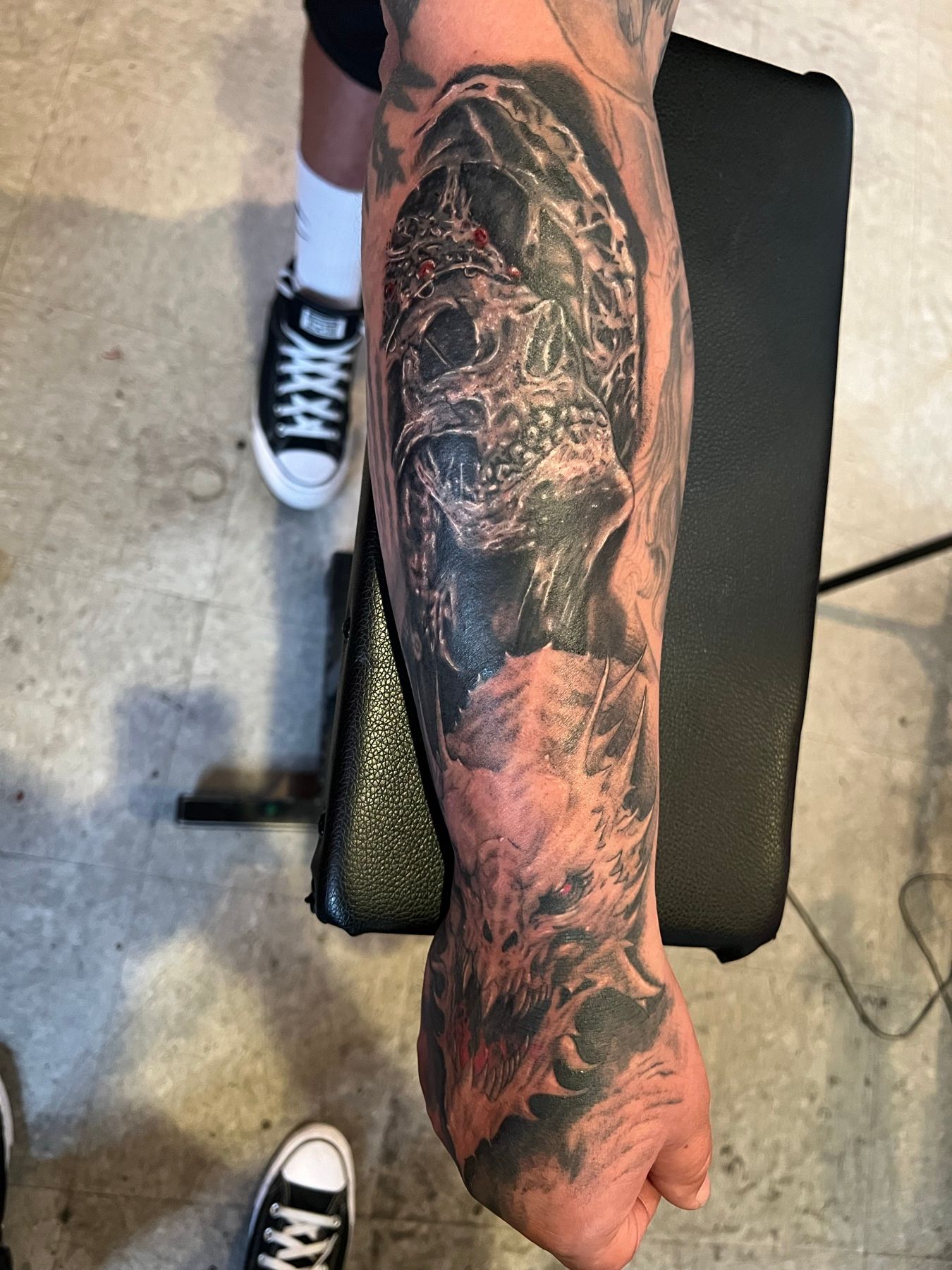 Black and grey realism sleeve tattoo of dark skulls and shadowed figures wrapping a forearm, by American Ink in Sherman Oaks.