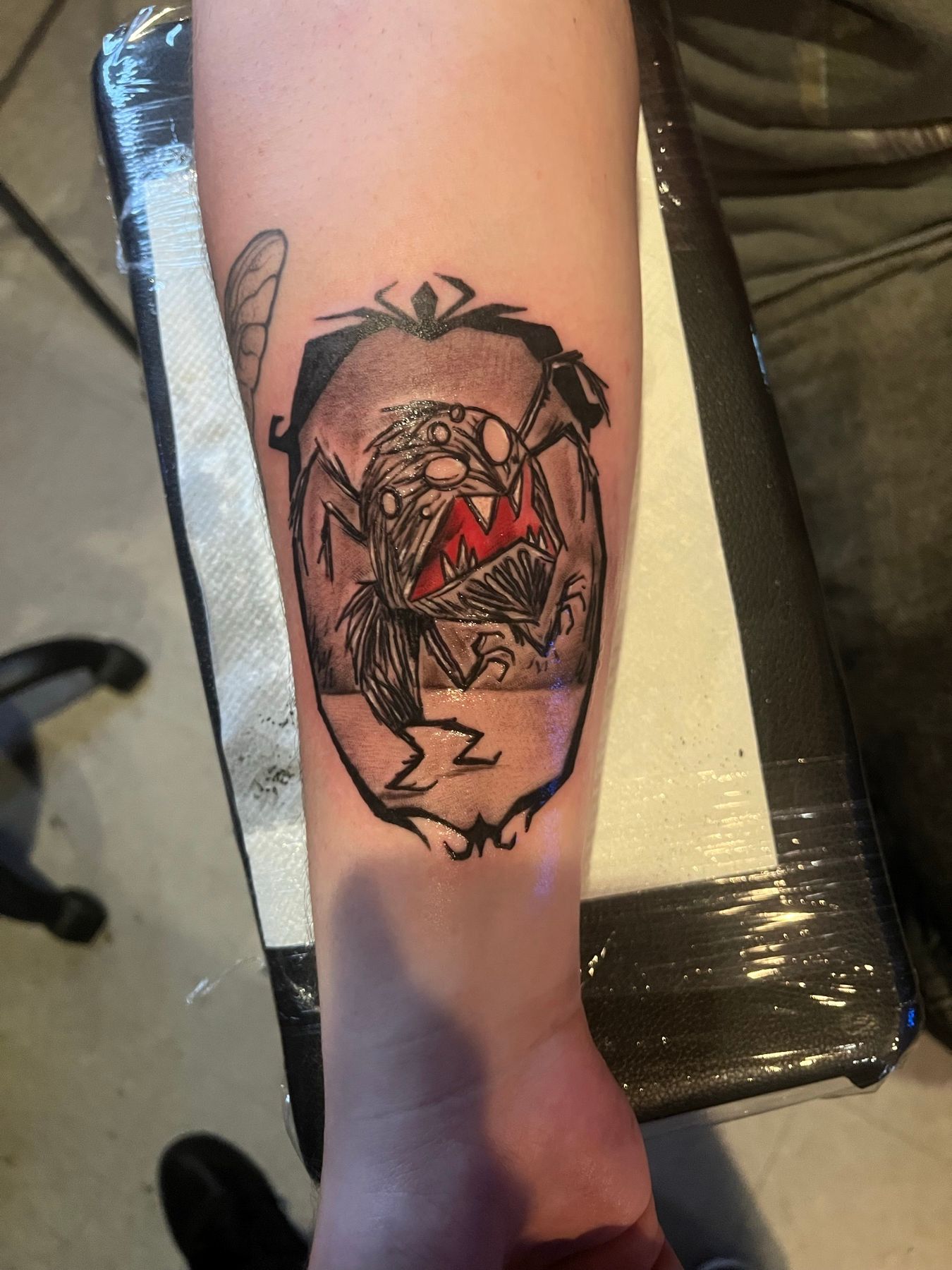 Color illustrative tattoo of a cartoon spider creature with a red gem on a forearm, by American Ink in Sherman Oaks.