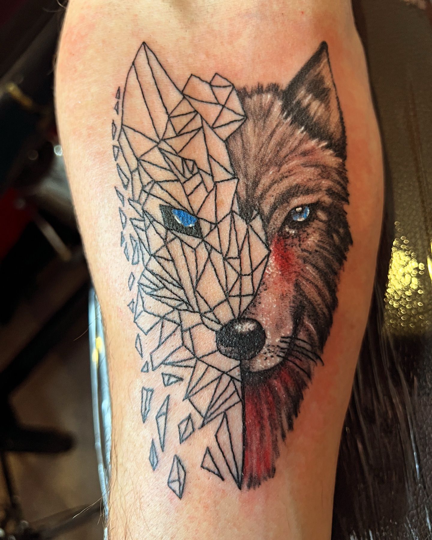 Geometric and black and grey realism tattoo of a wolf face split between linework and a shaded portrait with blue eyes on a forearm, by American Ink in Sherman Oaks.