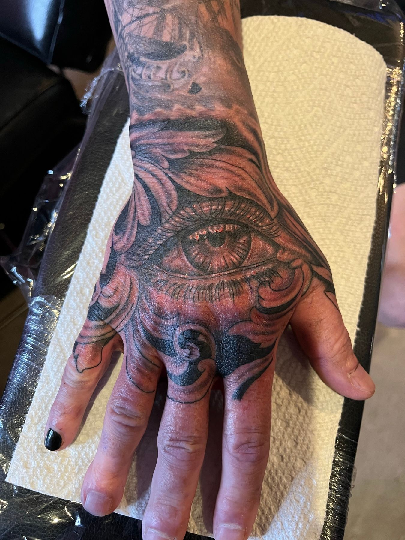 Black and grey ornamental tattoo of a realistic eye surrounded by baroque filigree scrollwork on the back of a hand, by American Ink in Sherman Oaks.
