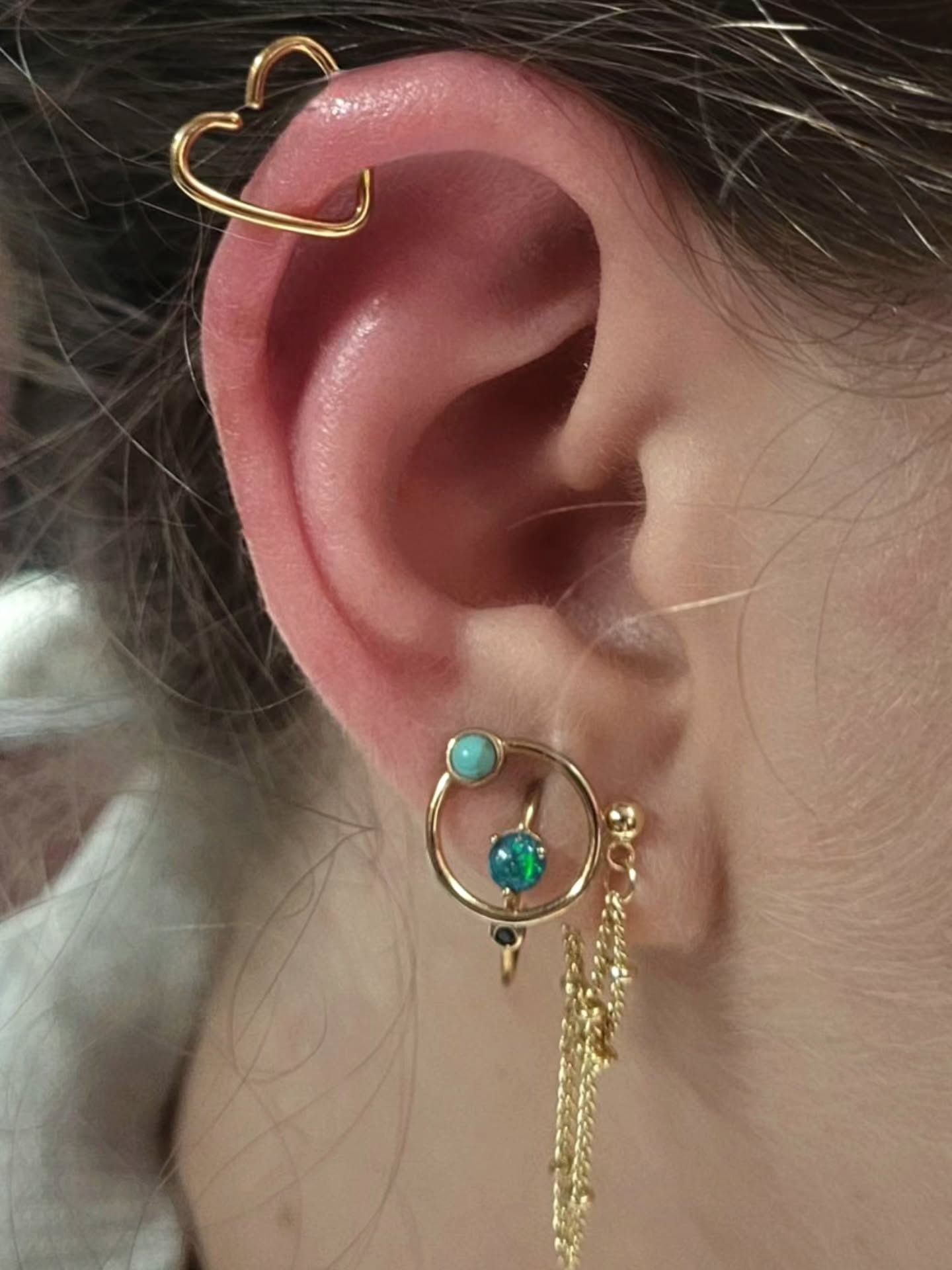 Curated ear at American Ink Sherman Oaks — a gold heart-shaped helix ring above lobe jewelry set with turquoise, opal, and a fine gold chain.