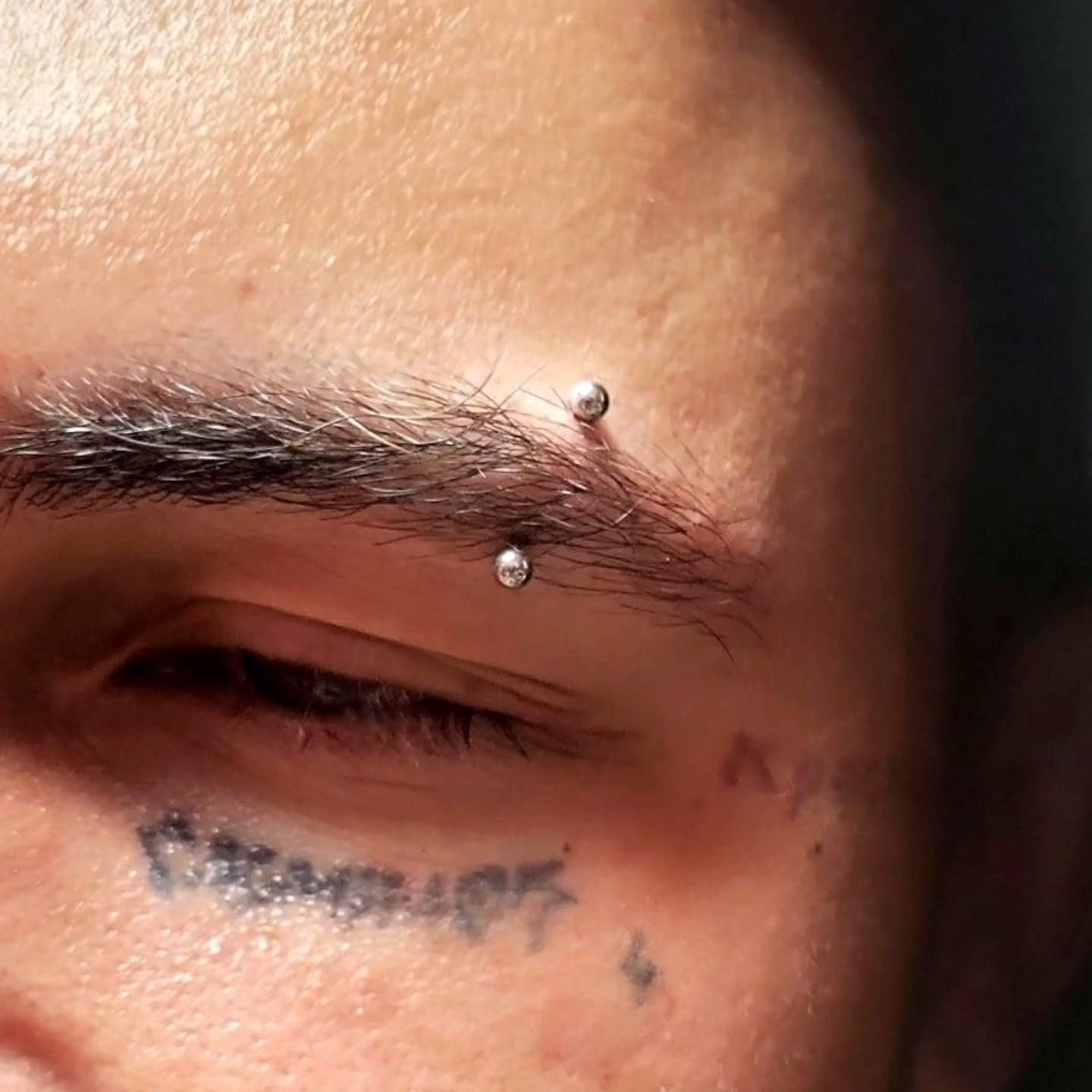Eyebrow piercing with a curved barbell and gem ends on a tattooed client, done by American Ink in Sherman Oaks.