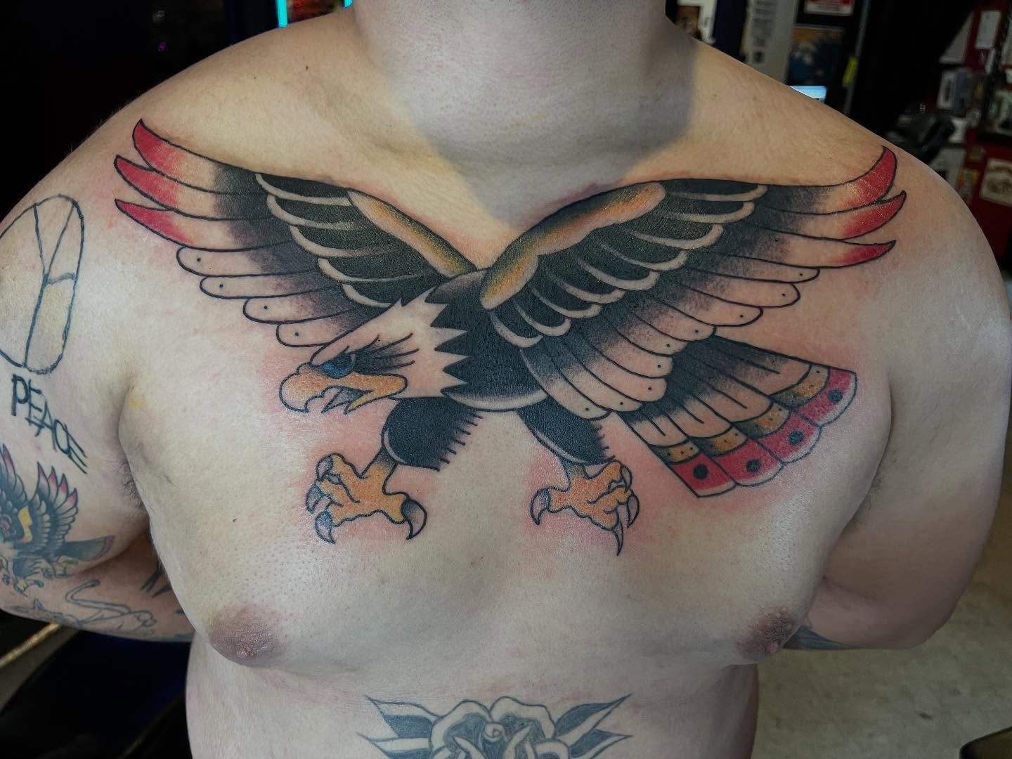 Color American traditional eagle chest tattoo with spread wings and red tail feathers, tattooed by Josue at American Ink in Sherman Oaks.