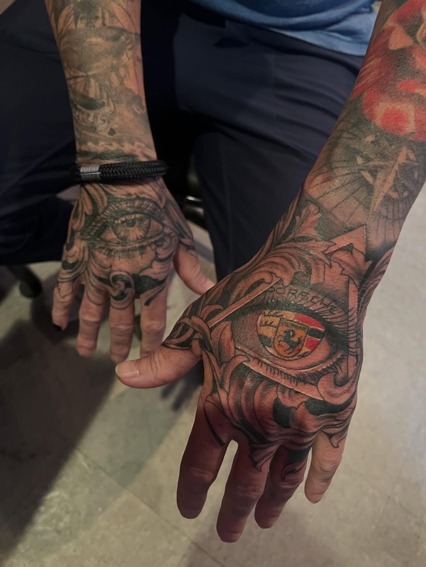 Matching ornamental hand tattoos with realistic eyes framed in filigree, one iris detailed with a color Porsche crest, by Josue at American Ink in Sherman Oaks.