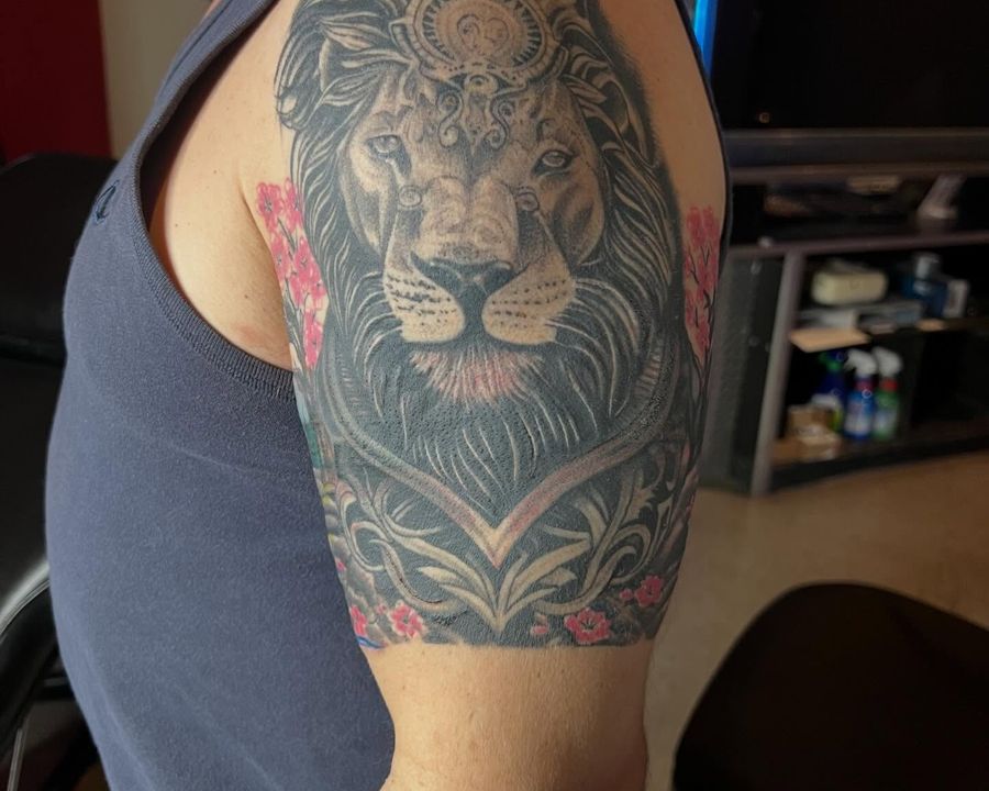 Ornamental lion half-sleeve with crown detail and floral color accents, tattooed by Josue