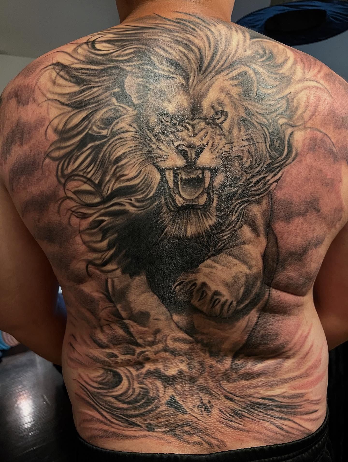 Full-back black and grey tattoo of a roaring lion charging through waves and clouds, tattooed by Josue at American Ink in Sherman Oaks.