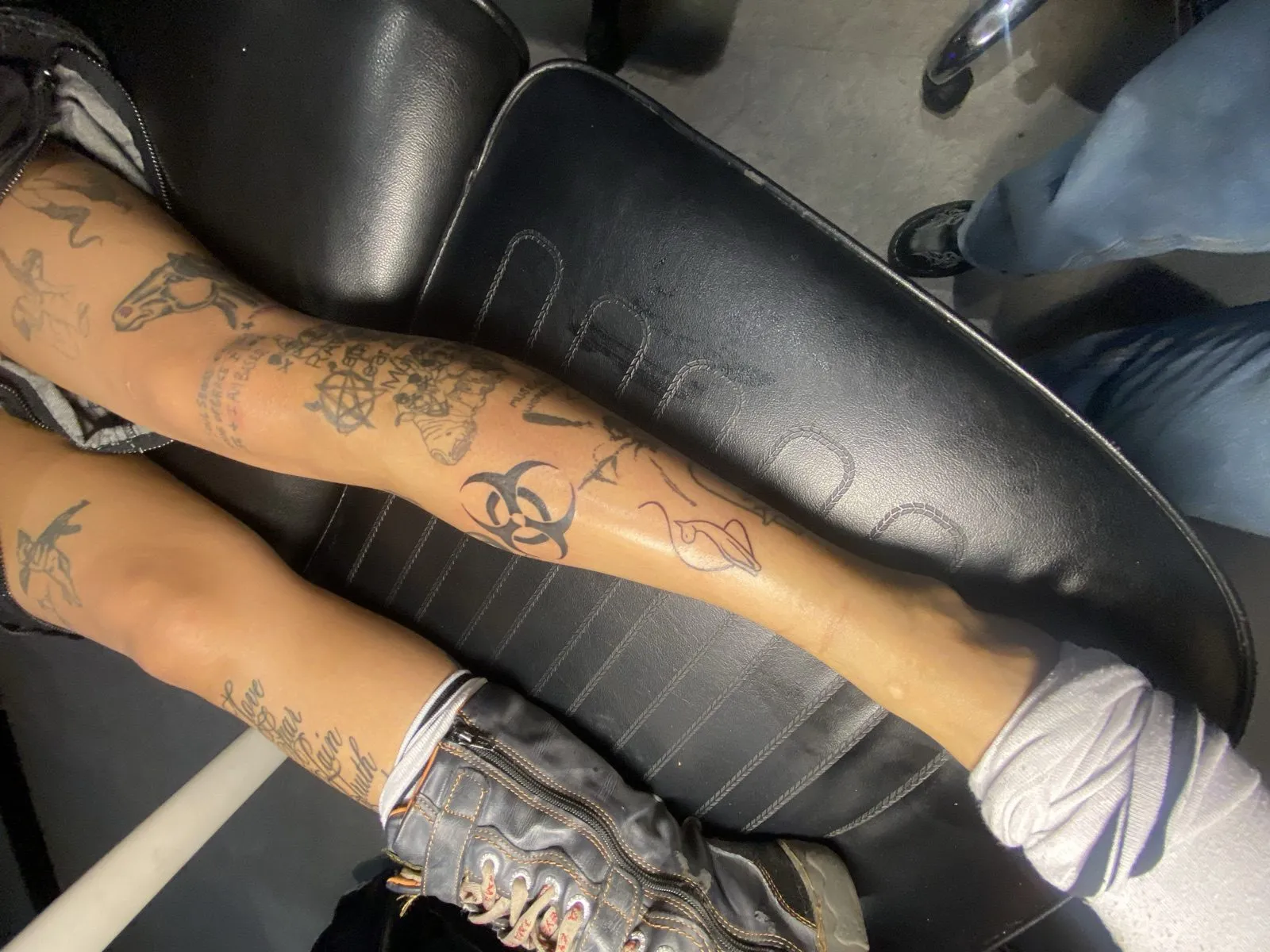 Patchwork of scattered fine-line tattoos across both lower legs by Knives, small black-ink pieces built up over time — tattoo work at American Ink in Sherman Oaks.