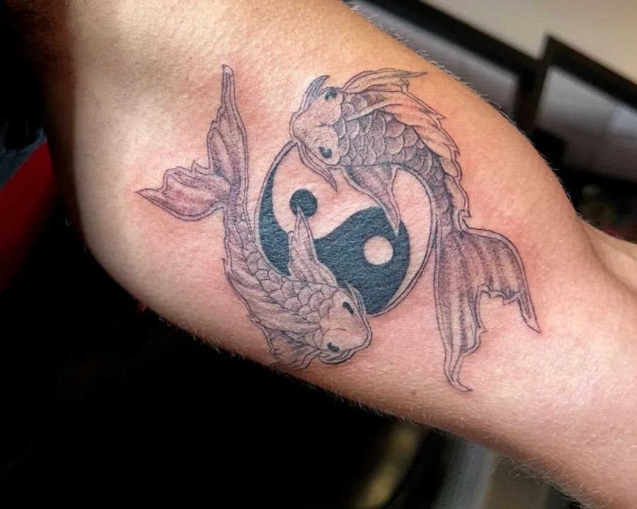 Finely shaded koi circling a yin-yang on the inner bicep, from the American Ink studio