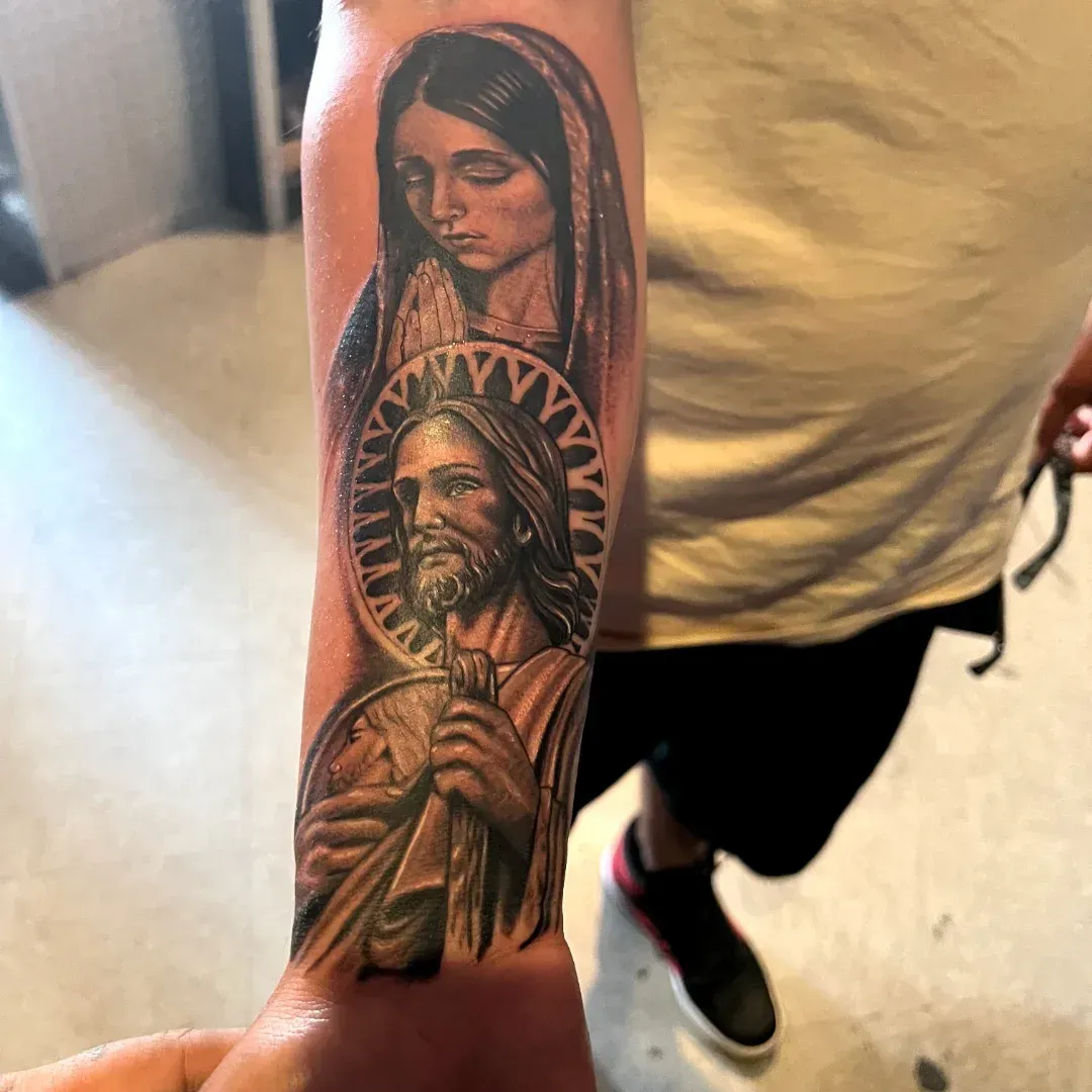 Black and grey religious forearm sleeve with the Virgin Mary praying above San Judas, from the American Ink studio in Sherman Oaks.