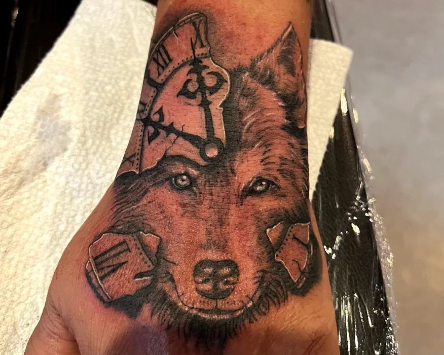 Wolf and broken clock hand tattoo in black and grey, from the American Ink studio