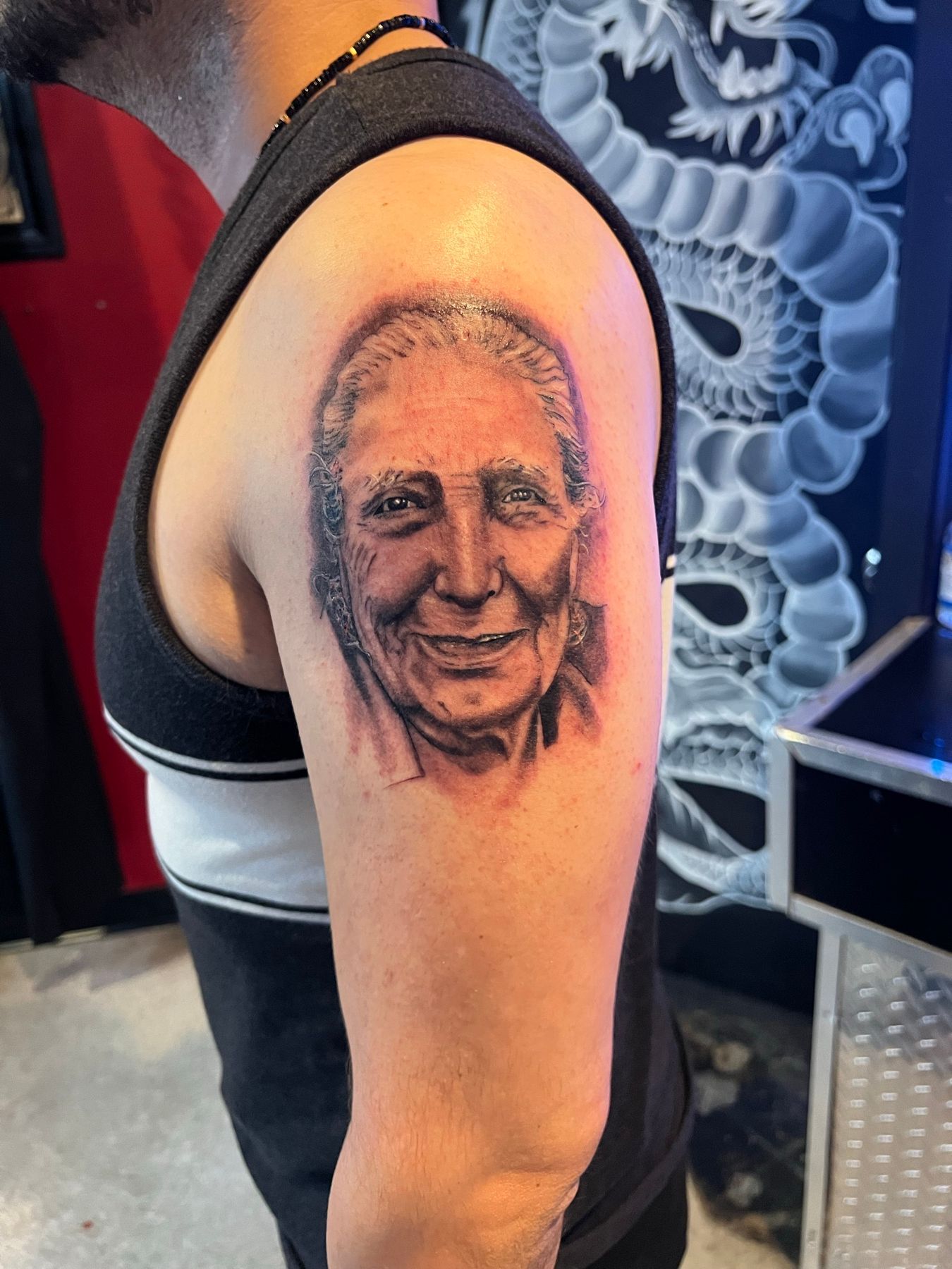 Black and grey realism upper arm tattoo portrait of a smiling man, by American Ink in Sherman Oaks.