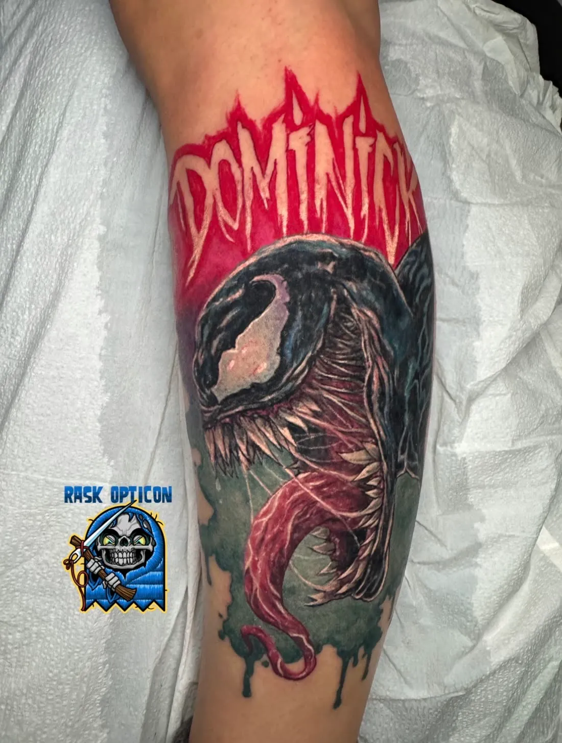 Color realism calf tattoo of Marvel's Venom beneath "Dominick" lettering, by Rask Opticon at American Ink in Sherman Oaks.