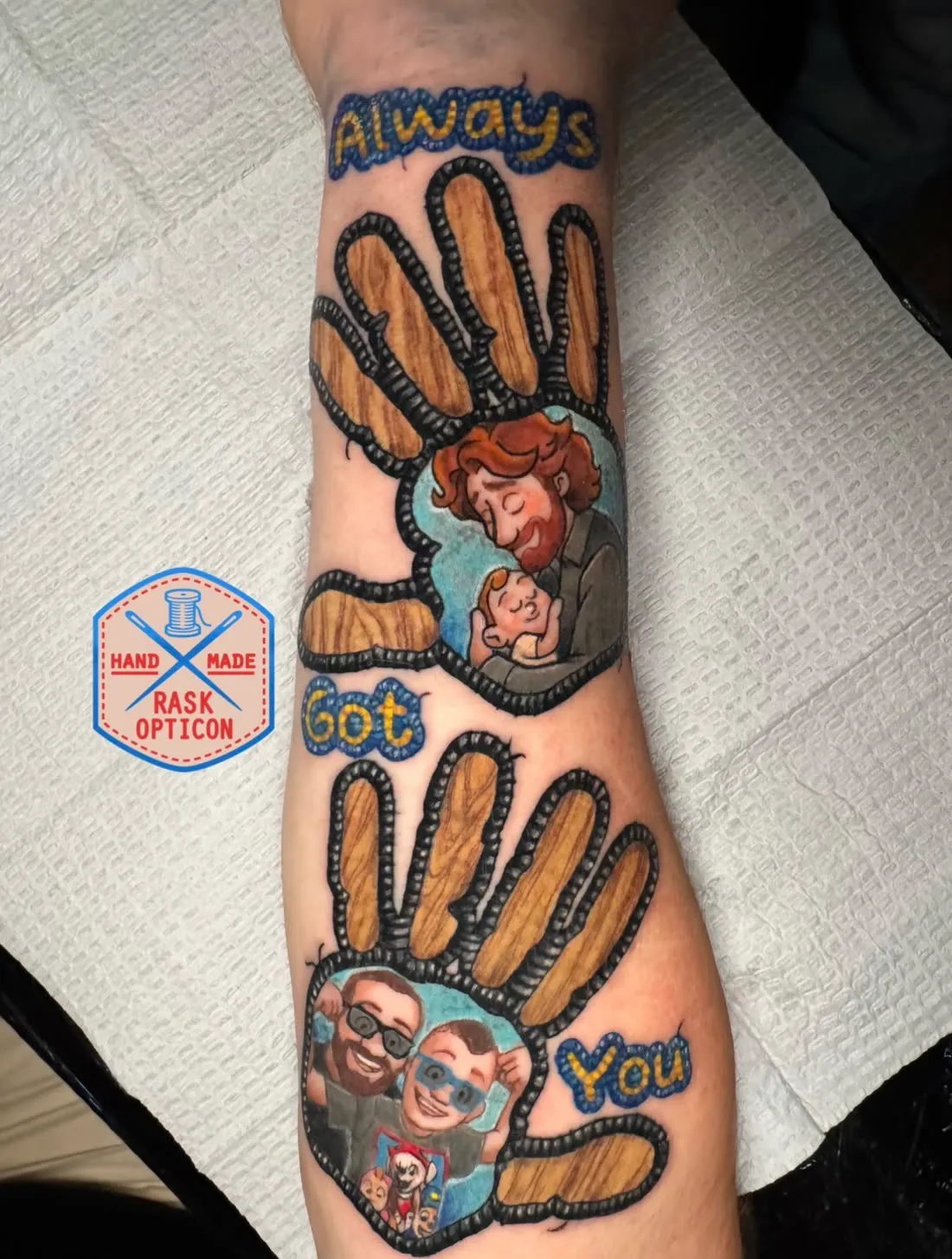 Embroidery patch-style memorial forearm tattoo of two woodgrain handprints reading "Always Got You" with cartoon family portraits, by Rask Opticon at American Ink in Sherman Oaks.