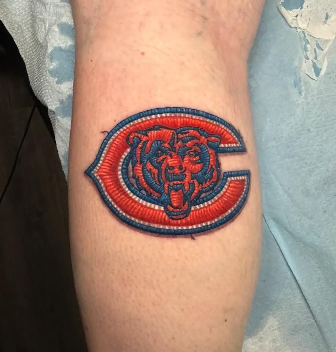 Embroidery patch-style tattoo of the Chicago Bears "C" bear-head logo in orange and blue thread, by Rask Opticon at American Ink in Sherman Oaks.