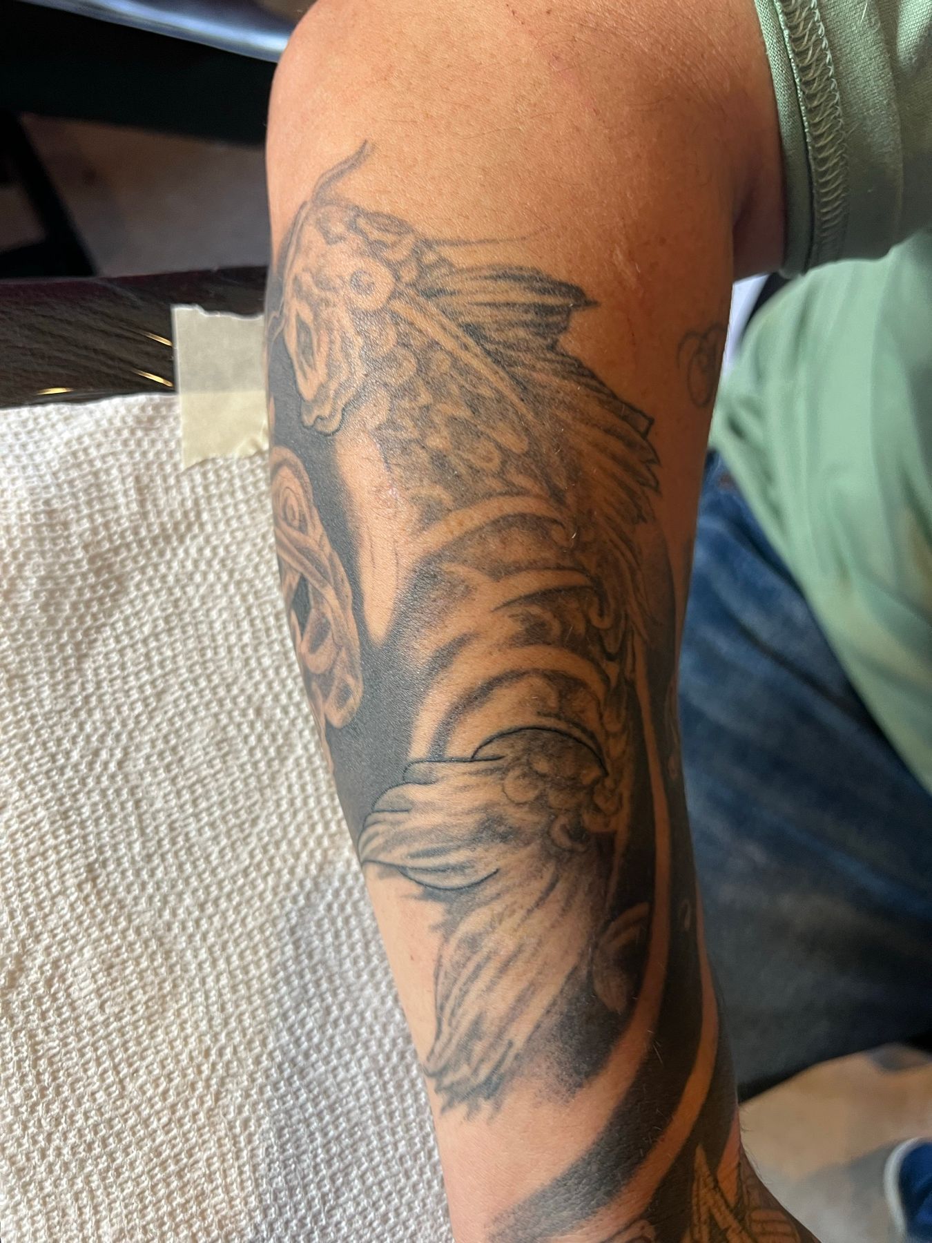 Old, faded black and grey koi fish forearm tattoo before being reworked at American Ink in Sherman Oaks.