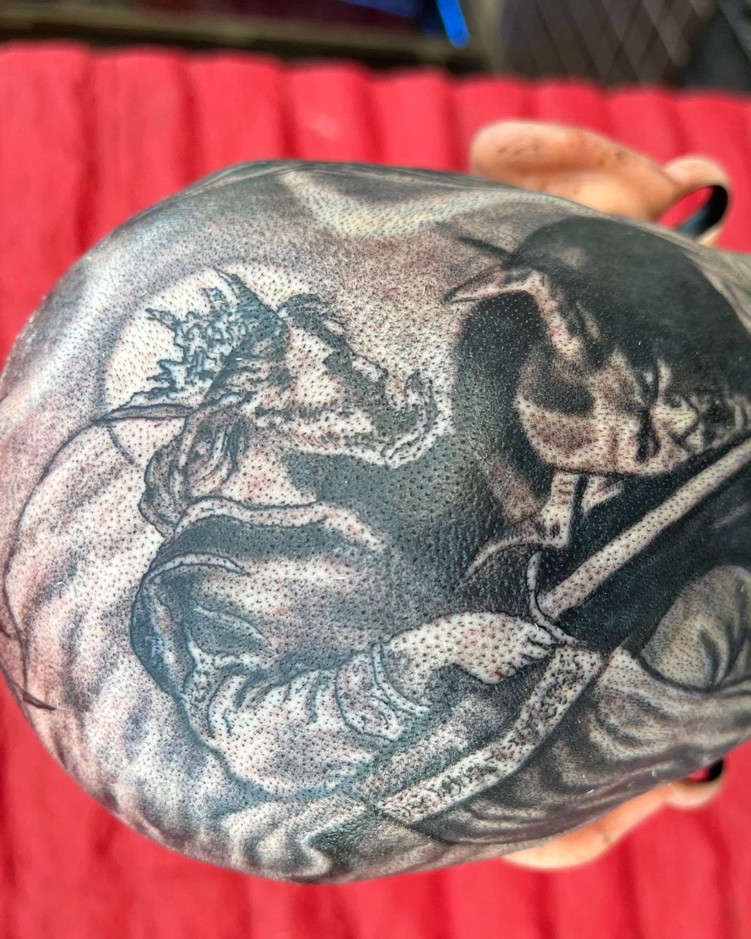 Black and grey scalp tattoo of a robed figure holding a sword across the back of the head, by American Ink in Sherman Oaks.